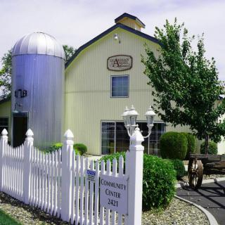 A quaint barn with a silo, surrounded by a white picket fence and greenery.