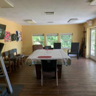 A spacious room with a dining table and chairs, decorated with artwork, featuring large windows that allow natural light to fill the space.
