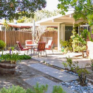 A serene backyard patio with outdoor furniture, surrounded by lush plants and a sunny atmosphere.