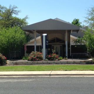 A small building surrounded by greenery seen from across the street.