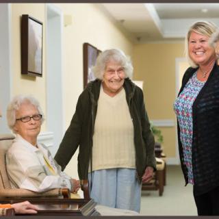 A group of elderly women and a caregiver in a nursing home setting.