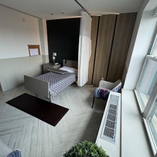A modern bedroom featuring a bed, chair, and large windows with natural light.