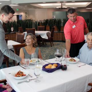 A group of people enjoying a meal at a restaurant with servers attending to them.