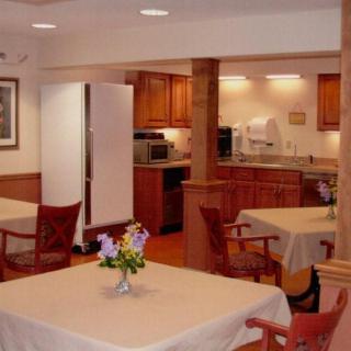 A cozy dining area with wooden tables and chairs, featuring a kitchen in the background.