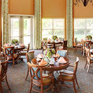 A well-decorated dining room featuring round tables with elegant place settings and large windows providing natural light.