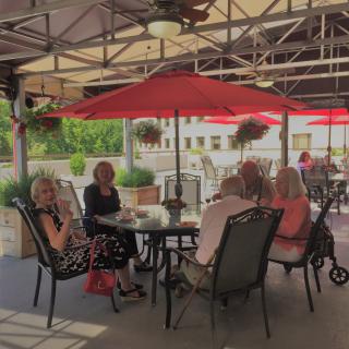 A group of people enjoying a meal together on a shaded patio with red umbrellas.