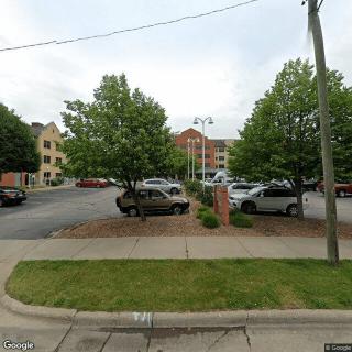 A parking lot with several cars parked, surrounded by trees and buildings on an overcast day.