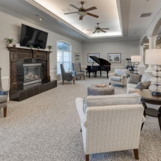 A spacious and elegantly decorated living room featuring a grand piano, comfortable seating, a fireplace, and a large TV.