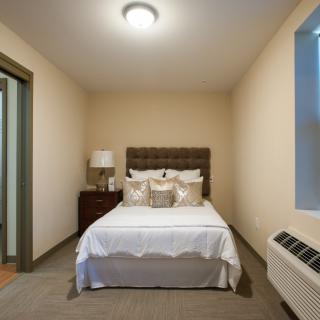 A cozy bedroom with a neatly made bed, bedside table, and a window.