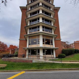 A modern brick building with multiple stories and large windows, situated on a green lawn by the street.