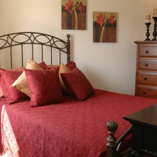 A cozy bedroom with red bedding and floral artwork on the wall.