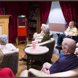 A group of seniors seated and attentively listening to a presentation in a cozy indoor setting.