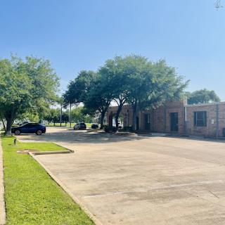 A serene view of a building surrounded by trees and a spacious parking lot under a clear blue sky.