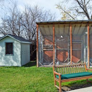 An outdoor scene with a bench in front of a small shed and an enclosed structure on a grassy area.