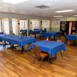 A dining area with blue tablecloths on several tables and a wooden floor.