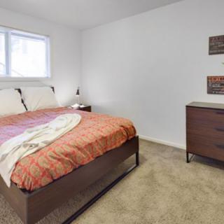 A cozy bedroom with a bed, dresser, and window on a carpeted floor.