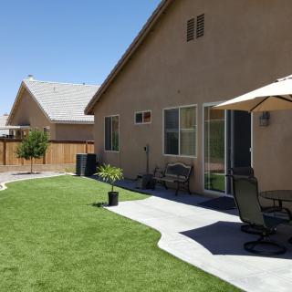 A sunny backyard featuring a patio with chairs and an umbrella, surrounded by a well-maintained lawn.