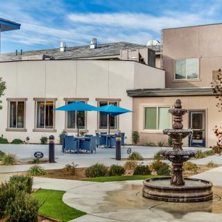 A modern building with outdoor seating and a central fountain surrounded by landscaped pathways.