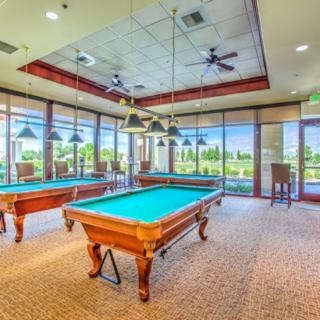 A spacious billiard room with multiple pool tables, large windows, and elegant lighting.