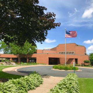 A brick building with an American flag flying, surrounded by lush greenery and a clear blue sky.