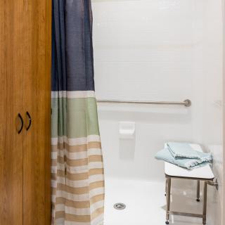 A simple bathroom with a shower area featuring a colorful curtain, towels on a rack, and a grab bar.