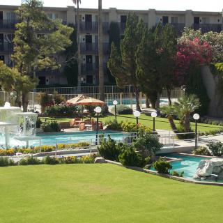 A sunny view of a hotel garden with a pool and fountain.