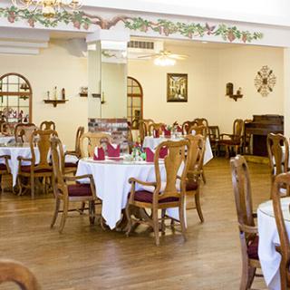 A spacious dining area with elegantly set tables and wooden chairs, featuring classic decor.