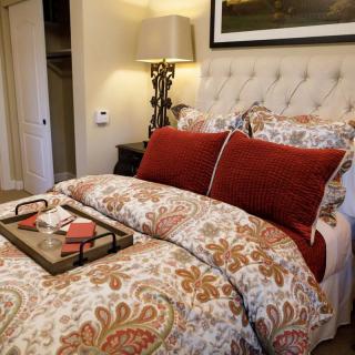 A cozy bedroom with a beautifully patterned duvet, red accent pillows, and a decorative tray on the bed.