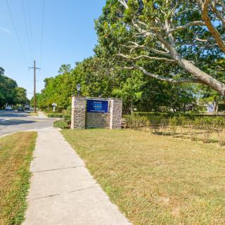 A sidewalk in a suburban area with a sign, trees, and a fence alongside the road.
