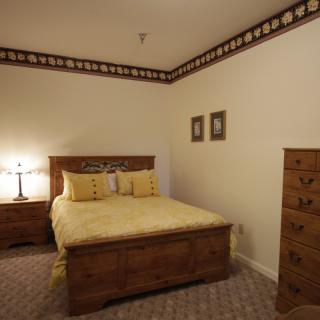 A cozy bedroom featuring wooden furniture, including a bed with yellow bedding, a nightstand with a lamp, and a tall dresser.