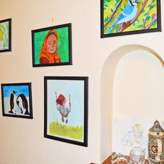 A collection of framed paintings displayed on a wall, featuring birds, animals, and portraits in a cozy interior setting.