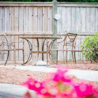 A serene patio area with a metal table and chairs, bordered by a wooden fence and bright pink flowers.