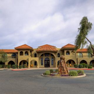 A Spanish-style building with a terracotta roof, framed by palm trees and a central statue at the entrance.