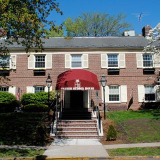 A brick building with a red awning covering the entrance, surrounded by greenery.