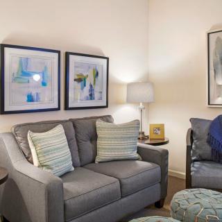 A cozy living room with a grey sofa, abstract artwork on the walls, and a standing lamp.