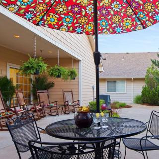 A cozy outdoor patio with a colorful umbrella, rocking chairs, and a table set for relaxation.
