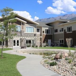 A modern residential building surrounded by landscaped grounds and a serene pond.