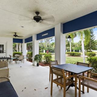 A spacious covered patio with tables and chairs, enhanced by ceiling fans and overlooking a lush garden.