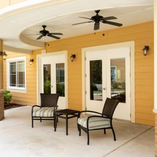 A cozy patio area with two chairs and a table, located outside a building with double doors and ceiling fans.