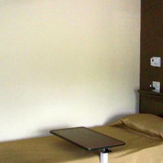 A hospital room with a single bed and adjustable table.
