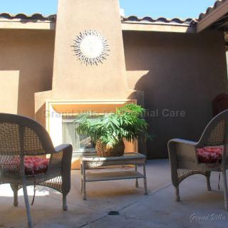 A cozy patio with wicker chairs and a fireplace, enhanced by sunlight and greenery.