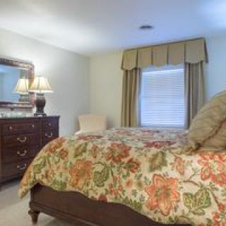 A cozy bedroom with a floral bedspread, wooden dresser, and soft lighting.