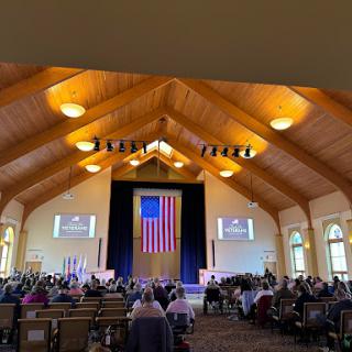 A congregational gathering in a beautifully designed wooden church interior, featuring an American flag as the focal point.