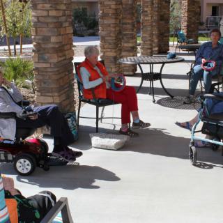 A group of seniors socializing outdoors on a sunny patio, with some using wheelchairs.