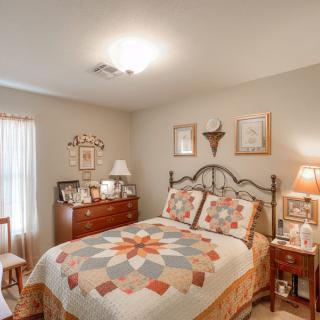 A cozy bedroom with a colorful quilt on the bed, wooden furniture, and tasteful decor.