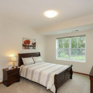 A cozy bedroom with a neatly made bed, nightstand, and a window providing natural light.