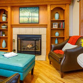 A cozy living room with a fireplace, armchair, and decorative shelves.