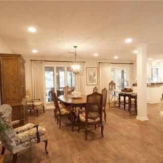 A spacious dining room with traditional decor, featuring a wooden dining table and chairs under a chandelier, complemented by a wooden floor and ceiling lights.