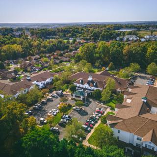 Aerial view of a building complex surrounded by lush greenery and a parking lot.