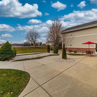 A peaceful outdoor patio area with a red umbrella and landscaped pathway beside a building under a partly cloudy sky.